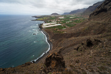 Rocky coast of the Atlantic Ocean. In the background, the small town of Buenavista del Norte. View from the observation deck - Mirador Punta del Fraile. Tenerife. Canary Islands. Spain.