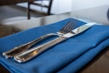 Angled view of a fork and knife placed delicately on a royal blue cloth napkin on a wooden table...