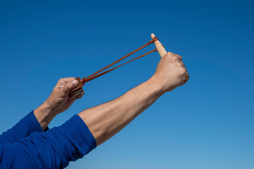 Hands of a man stretching the elastic band of a slingshot. - obrazy, fototapety, plakaty