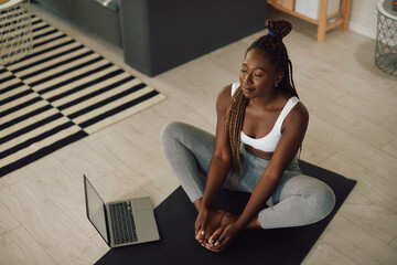 Young black woman does breathing exercises during online Yoga class at home.