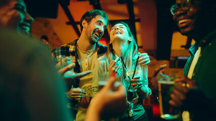 Carefree couple laughs while being on party in pub at night.