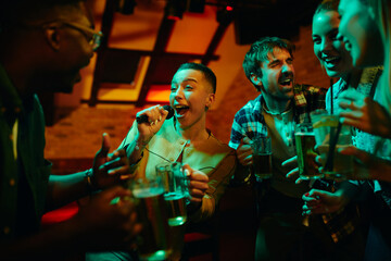 Group of carefree friends sing and have fun on night karaoke party in bar.