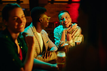 Happy African American woman and her boyfriend talk while drinking beer in pub.