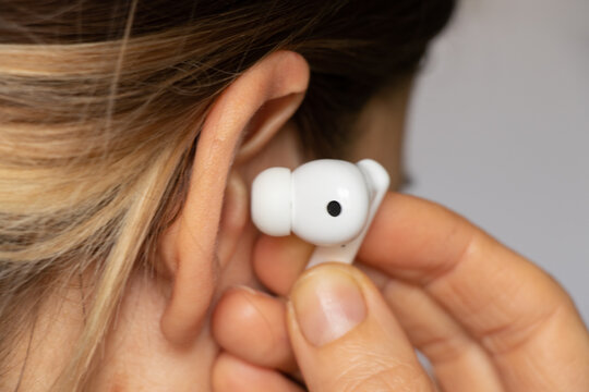 Wireless TWS white headphones in a girl's ear close-up, listening to music in headphones