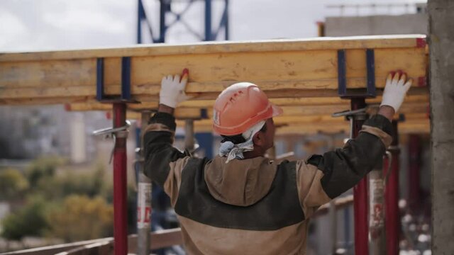 a worker in a helmet installs a beam on a construction site