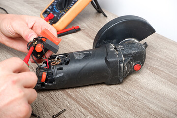 Power tool repair. A man repairs an angle grinder. Screwdriver, multimeter. Details of electrical...