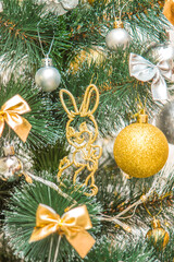 Hanging squirrel figure decoration on the Christmas tree. Gold and silver baubles, multi-colored bows, bells, lit garlands against the decorative brick wall background. Close-up, selective focus