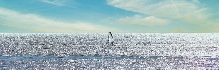 Windsurfer sailing through a silver sea in a sunny day