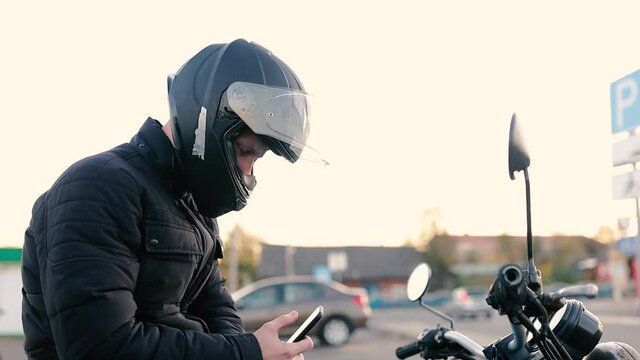 motorcyclist on a bike in a helmet uses a smartphone while sitting on a motorcycle. application for motorcyclists.
