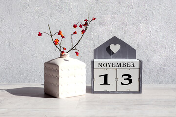 Calendar for November 13: the name of the month in English, the number 13 on cubes, a branch with red fruits in a white vase, shadows from objects, gray background