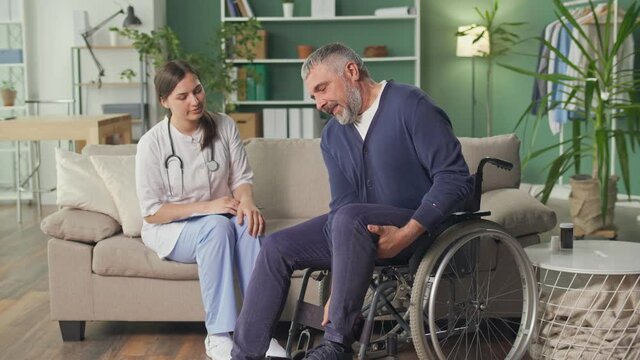 A Caring Nurse Assists a Middle-aged Man in a Wheelchair at Home. Rehabilitation, Medical Care, Health Support, Social Assistance, Doctor and Home Services.