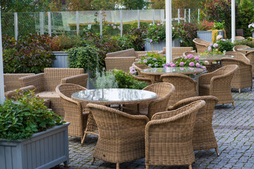 Garden cafe terrace decorated with outdoor wicker furniture and growing flowers in pots. Empty street patio or restaurant interior with fresh blooming potted plants for summer entertainment visits