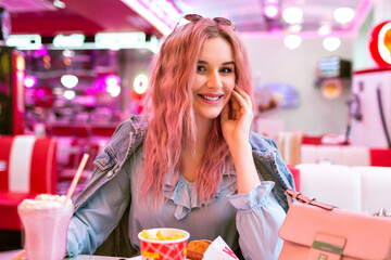 Positive lifestyle portrait of happy exited pretty woman with pink hairs having dinner