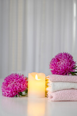Set of fresh towels of pink and white color with purple aster flowers and candle on white table. Hotel spa and wellness concept. Copy space.