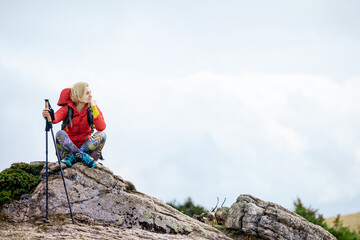 Hiker girl taking a rest on a rock in the mountains. Windy day. Travel and healthy lifestyle...