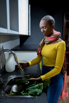 Young African American woman wearing a yellow shirt washing vegetables at home
