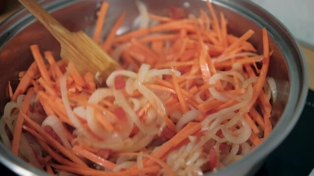 Wooden spoon stirring yam, carrots, tomato, and onion slices in pot