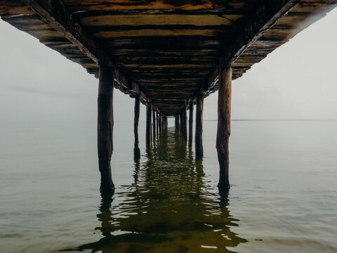 Symmetrical view underneath a wooden pier with still water