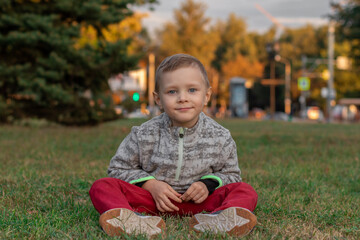 little cute boy sitting on the grass outside and smiling at the camera