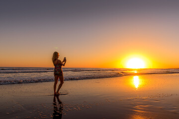 Fototapeta na wymiar Woman on the beach photographing the sunset