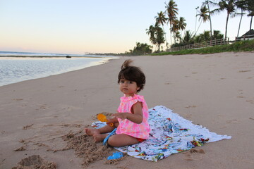 criança brincando na areia da praia com uma pazinha
