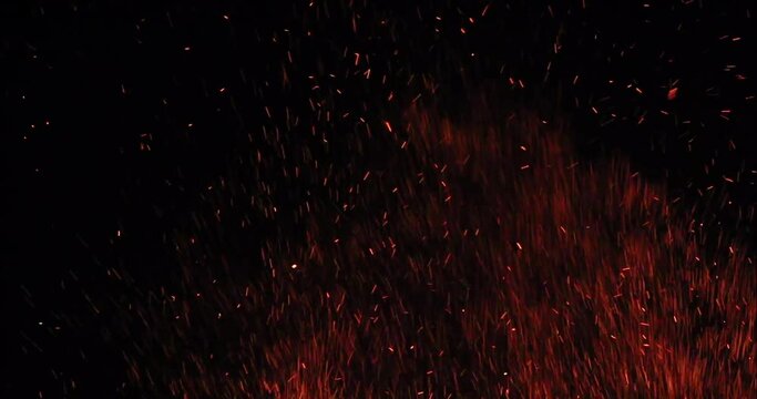 Bonfire sparkles rising in the air during a dark night.