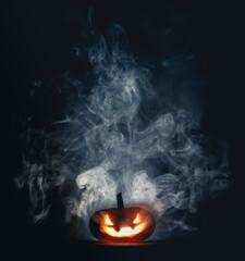 Spooky Halloween jack o lantern pumpkin with carved scary grinning face glowing in smoke on...