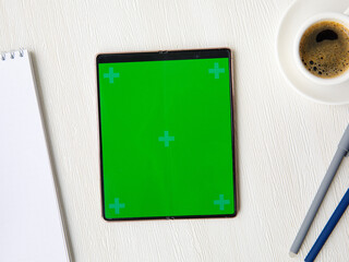 New folding Smartphone Samsung Galaxy Z Fold 2 with green screen, open notebook, cup of coffee, pens lying on white table. Flat lay top view, mock up. October 4 ,2021 Novosibirsk,Russia