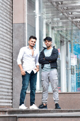 Two male models posing for fashion photoshoot. Men at city street smiling at the camera