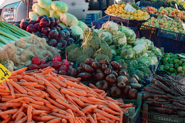 A vibrant farmers' market stall displaying fresh carrots, beets, and cabbages. The colorful array of vegetables highlights the freshness and variety available at local markets. Horizontal shot