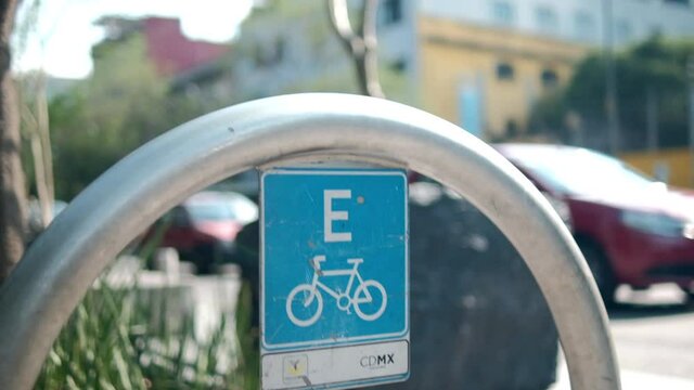 Blue bicycle parking spot sign on metal arch with traffic as background