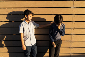 Caring for sad child. Two young boys standing resolving conflict. Giving help concept. Kid giving Support. Golden hour scene of upset child with hand on face. Hand on shoulder.