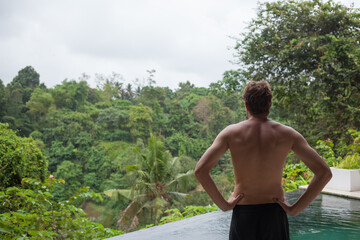 man standing at pool side enjoying view of jungle