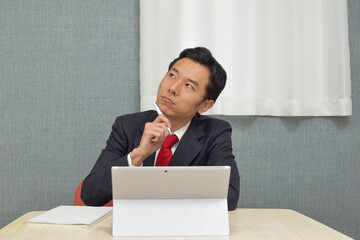 A young Asian man wearing business suit thinks about new idea and writes some memos on his notebook during telework at home