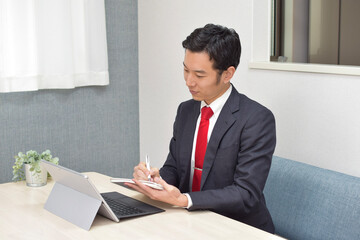 A young Asian man takes a memo on his note during telework at home