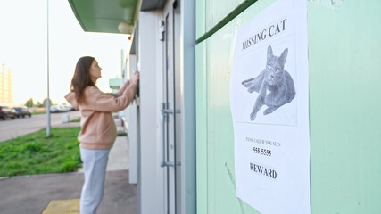 Upset female owner in beige hoodie hangs posters of missing cat with picture on green walls on...