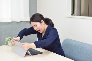 A young Asian woman gets angry at her colleague and shows her emotion holding a pc with her hands during telework