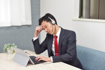 A young Asian man wearing a headset is in trouble during meeting with customers and do telework at home