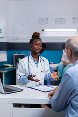 Obraz premium African american doctor discussing checkup results with old patient sitting in healthcare office. Black medic talking to elderly man with disease about professional examination at appointment