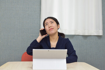 A young Asian woman during telework at home talks on her phone and thinks about how to answer to his client