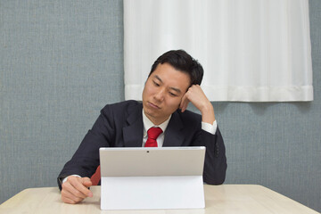 A young Asian man wearing business suit is in trouble and thinks about how to solve it during telework at home