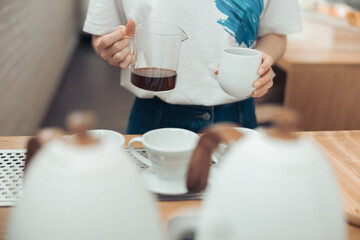 Female barista holding glass mug and cup of coffee
