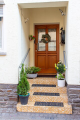 Fototapeta na wymiar Close up view of a European entryway door and steps, with beautifully landscaped flower pots and a wreath