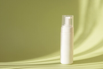 White bottle with dispenser on green background, in rays of sunlight. Mock up of packaging for cosmetic lotion, cleansing foam for washing. Concept of beauty industry