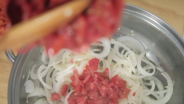 Pouring chopped tomatoes to cooking pot with onion slices