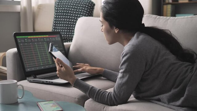 young woman lying on sofa trading online using tablet computer,female brunette trader using stock markets application to trade from home,people finance investment