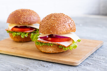 two burgers with ham tomatoes and cheese salad on a wooden board