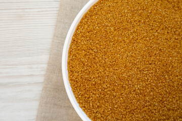 Organic Brown Sugar in a White Bowl on a white wooden surface, top view. Flat lay, overhead, from above. Copy space.