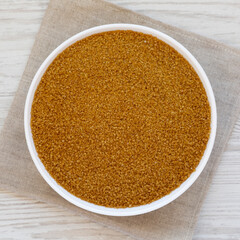 Organic Brown Sugar in a White Bowl on a white wooden surface, top view. Flat lay, overhead, from above.