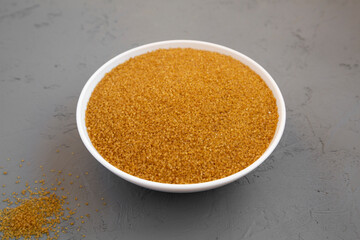 Organic Brown Sugar in a White Bowl on a gray background, low angle view.